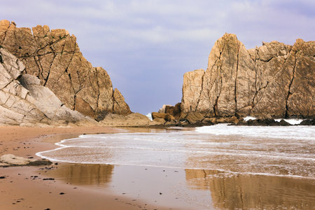 The Playa de la Arnia beach. The smooth wet sand of the beach reflects the rocky boulders. Snow-white sea foam glistens. Spain, Cantabriaの写真素材