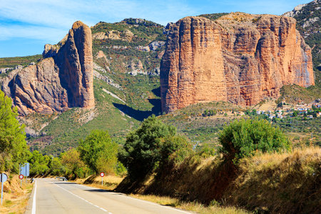 Asphalt highway passes through the rocks. Hoya de Huesca, Aragon. Part of the foothills of the Pyrenees. The Mallets of Riglos. Sunny afternoon. Romantic trip to Spain.の写真素材