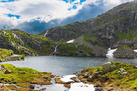 Last year's snow and gray skies. Cold summer in Norway. Large snowfields is reflected in the water of the lake. Traveling by camper on road 520.の写真素材