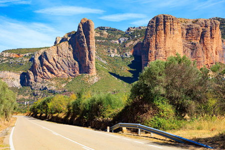 Asphalt highway passes through the rocks. Part of the foothills of the Pyrenees. The Mallets of Riglos. Hot sunny afternoon. Romantic trip to Spain. Hoya de Huesca, Aragon.の写真素材