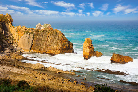 Playa de la Arnia beach. Amazing geological formations amaze tourists. Storm waves break on the coastal rocks. Snow-white sea foam glistens in the dim autumn sun. Cantabria, Spain.の写真素材