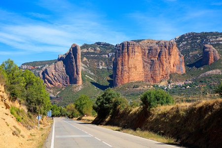 Asphalt highway passes through the rocks. Hoya de Huesca, Aragon. Part of the foothills of the Pyrenees. The Mallets of Riglos. Hot sunny afternoon. Romantic trip to Spain.の写真素材