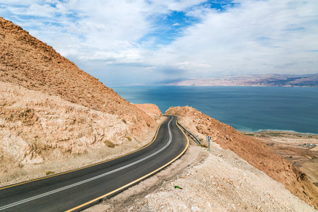 Gorgeous paved road along the seashore. The most salty sea on earth - Dead Sea. The Judean Desert is one of the most famous deserts in the world.  Israel, winter cloudy day.の写真素材
