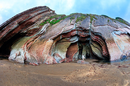 Huge cave on the beach. Woman doing yoga. Low tide in the Atlantic. Flysch - unique landscape of underwater rocks exposed at low tide. Playa Zumaya.の写真素材