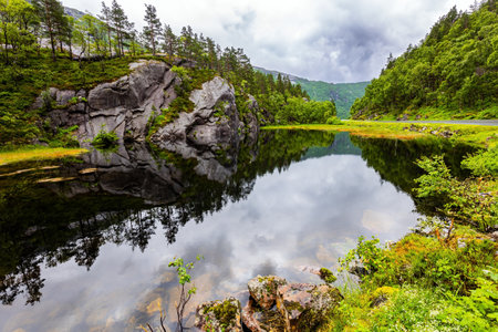 Bright reflections of the sky and clouds in the water. Scenic landscape in Western Norway. Summer cold and rainy day. Quiet small lake next road to Roldalの写真素材