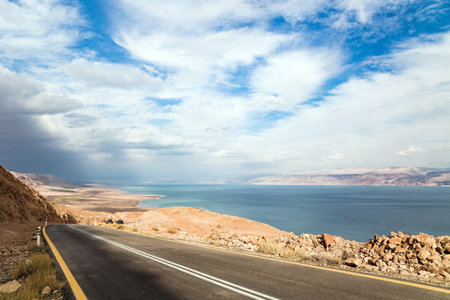 Paved highway along the seashore. The Judean Desert is one of the most famous deserts in the world. The most salty sea on earth - Dead Sea. Israel, winter cloudy day.の写真素材