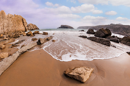 Interesting original rock ledges on the Playa de la Arnia beach. Cantabria, Spain. Picturesque geological formations amaze tourists. Snow-white sea foam glistensの写真素材