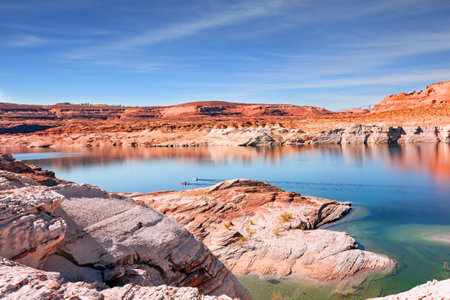 Lake Powell. The water reflects the surrounding shores. The smooth emerald water of the lake contrasts with the bright red terracotta sandstone shores. USA. The coast is cut by narrow canyons.の写真素材
