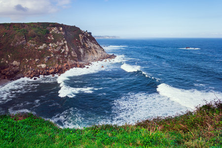Huge waves of surf beat against stone breakwaters. Magnificent Atlantic Ocean. Asturias. Picturesque fishing port of the city of Luarca in the bay. Romantic trip to Spain.の写真素材