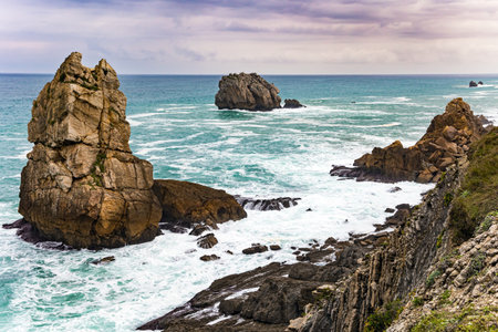 Portio beach. Stormy autumn day in the Bay of Biscay. The high surf crashes against the shore. Picturesque cliffs and huge stones oppose the ocean.の写真素材