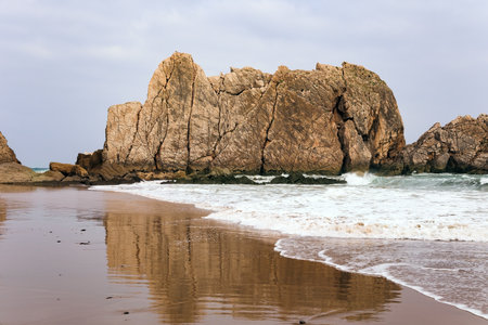 The Playa de la Arnia beach. The smooth wet sand of the beach reflects the rocky boulders. Snow-white sea foam glistens. Cantabria, Spainの写真素材