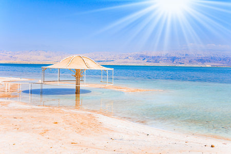 Coast of Israel. Evaporated salt forms Ñrystals on the surface of the water. The Dead Sea is an endorheic, very salty lake in the Middle East. Lovely umbrella protects from the sun.の写真素材