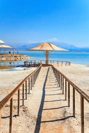 Lovely round umbrella protects from the sun. The drainless salt lake in the Middle East. Dead Sea. Coast of Israel. Railings enclose the path to the waterの写真素材