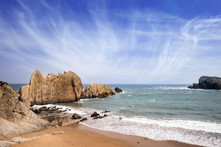 Snow-white sea foam glistens in the dim autumn sun. Cantabria, Spain. Playa de la Arnia beach. Amazing geological formations amaze tourists. Storm waves break on the coastal rocks.の写真素材