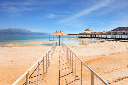 Railings enclose the path to the water. Lovely round umbrella protects from the sun. The drainless salt lake in the Middle East. Dead Sea. Coast of Israel.の写真素材