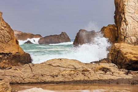 Snow-white sea foam glistens. Cantabria, Spain. The rocky boulders. The Playa de la Arnia beach. Picturesque geological formations amaze tourists.の写真素材
