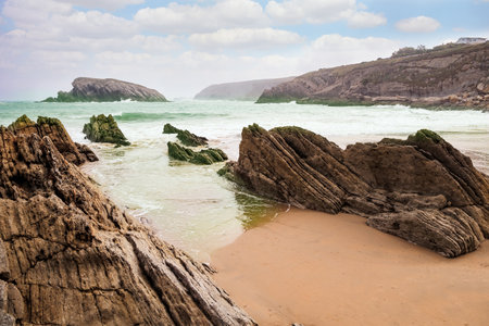 The rocky boulders. The Playa de la Arnia beach. Snow-white sea foam glistens. Cantabria, Spain. Picturesque geological formations amaze tourists.の写真素材