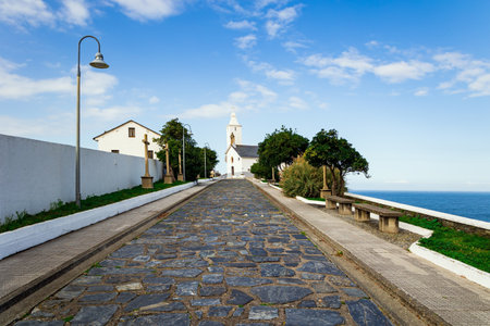 Beautiful stone paved highway. Watchtower Chapel and Lighthouse. Atlantic coast, Asturias. Unusual impressive architecture of the Luarca. Romantic trip to Spain.の写真素材