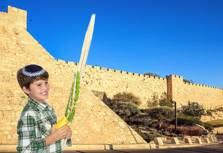 Handsome boy in a white kippah with lulav in his hands. Protective powerful walls of the Old City of Jerusalem at sunset. Jerusalem is the capital of Israel.の写真素材