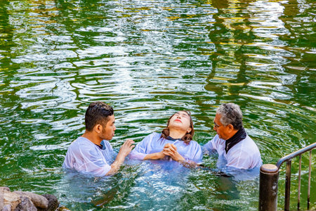 YARDENIT, ISRAEL - JANUARY 21, 2023: Happy pilgrims in baptismal shirts receive baptism in the cold water of the Jordan River. Yardenit is baptism center for Christians. Sunny winter day.のeditorial素材