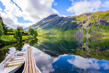 Pier with boat. Shallow lake Eidsvatnet in the mountains of Norway. The water reflects lush clouds, blue skies and forested shores. Summer in Scandinavia.の写真素材