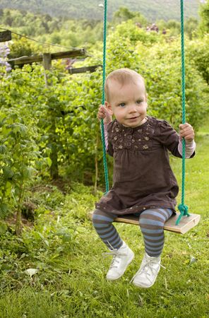 Sweet little blue eyed toddler on swing in a green gardenの写真素材