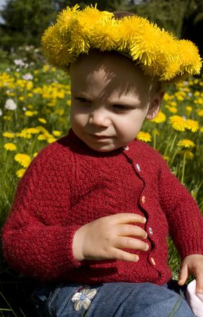 Toddler sitting in a flower field, with a yellow dandelion wreath.の写真素材