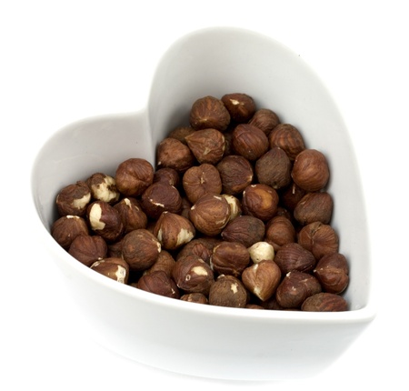 Brown roasted hazelnuts in a heart shaped bowl isolated on whiteの写真素材