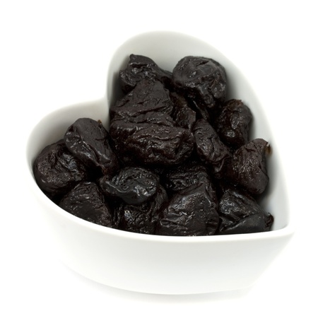 Prunes in a heart shaped bowl isolated on white backgroundの写真素材