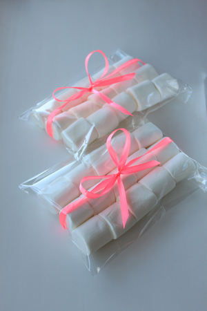 Marshmallows on white background with copyspace. Flat lay, top view. White chewing marshmallow in a gift transparent bag with a pink ribbon. A gift for the woman he loved, sweets.の写真素材