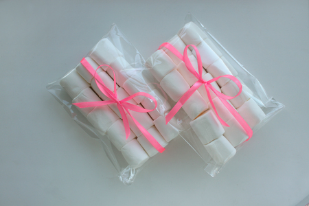 Marshmallows on white background with copyspace. Flat lay, top view. White chewing marshmallow in a gift transparent bag with a pink ribbon. A gift for the woman he loved, sweets.の写真素材