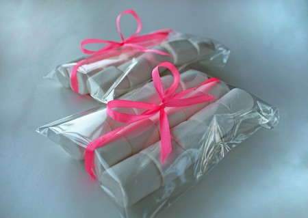Marshmallows on white background with copyspace. Flat lay, top view. White chewing marshmallow in a gift transparent bag with a pink ribbon. A gift for the woman he loved, sweets.の写真素材