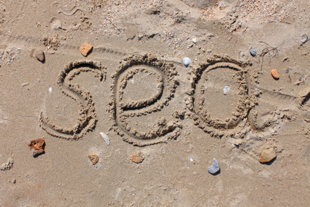 The inscription on the sand - Sea. Seashells, smooth stones and glass on the beach. Sunny day, summer vacation, weekend.の写真素材