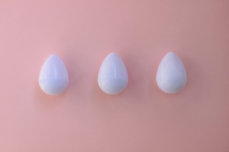 White eggs on the background in pink pastel color. Three small plastic toy eggs. Kids toys. Minimalism food concept. Easter concept.の写真素材