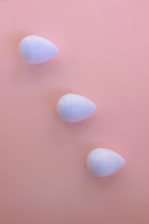 White eggs on the background in pink pastel color. Three small plastic toy eggs. Kids toys. Minimalism food concept. Easter concept.の写真素材