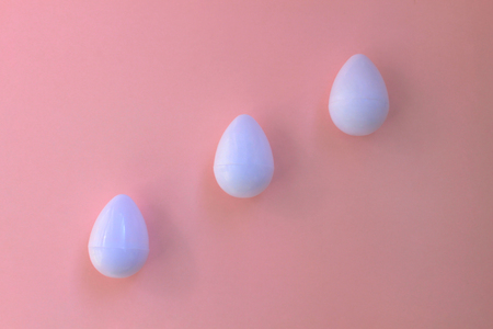 White eggs on the background in pink pastel color. Three small plastic toy eggs. Kids toys. Minimalism food concept. Easter concept.の写真素材