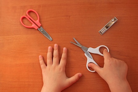 Special scissors for kids with rounded tips and nail clippers. Hand and nail care for the child. Children's manicure. Wooden background. Top view. Flat lay.の写真素材