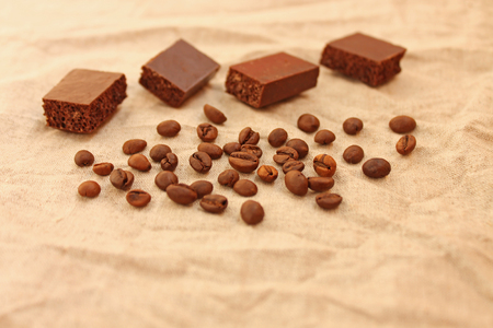 Milk porous chocolate cubes with coffee beans on a linen texture background. Sweets and coffee. Copy space. Selective focus.の写真素材