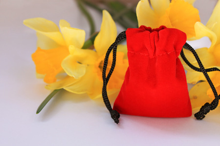 Red velvet pouch with yellow flowers on a white background isolated. Jewerly gift bag, cover for wedding rings. Bright daffdils. Declaration of love.の写真素材