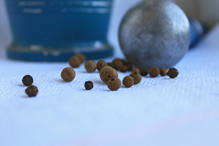 Black peppercorns ans allspice in ancient metal mortar with pestle on linen background. Old home kitchen appliances for grinding spices, nuts, herbs, coffee beans and others.の写真素材