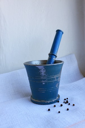 Black peppercorns ans allspice in ancient metal mortar with pestle on linen background. Old home kitchen appliances for grinding spices, nuts, herbs, coffee beans and others.の写真素材