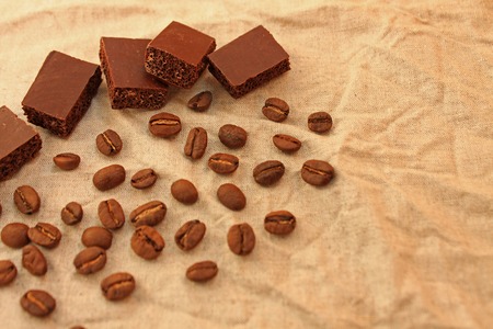 Milk porous chocolate cubes with colombian coffee beans on a linen texture background. Sweets and coffee. Copy space. Selective focus.の写真素材