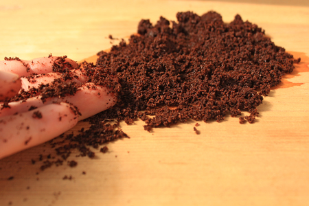 Coffee scrub for face and body, mask, cosmetics and care. Wet ground coffee in a hand on wooden background. Tablet of freshly prepared espresso.の写真素材