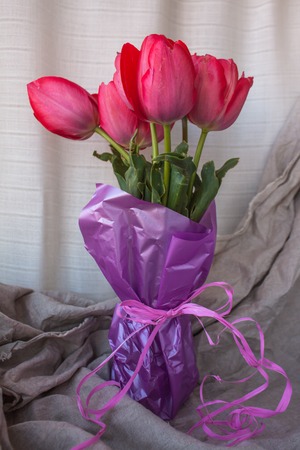 Fresh tender pink tulips in a vase with violet paper and ribbon bow on the background of crumpled linen fabric, copy space.の写真素材