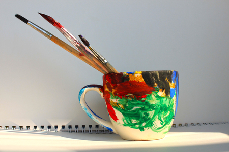 Art brushes in a painted cup on the white background, copy space, bright colours.の写真素材