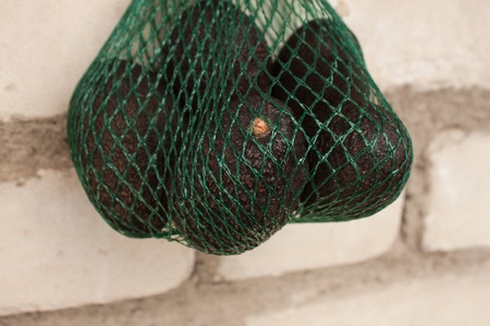 Fresh organic   avocados in a green string bag on a brick wall background, creative healthy food concept, copy space. Eco lifestyle, how to choose fruits and vegetables. Shopping, market.の写真素材