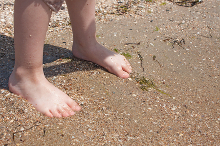 A baby try to step in to the sea water at the first time in a sunny day. Sea background, kids legs, family summer res, vacation with kids, sunburn, children's tan, swimming.の写真素材