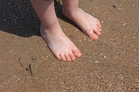A baby try to step in to the sea water at the first time in a sunny day. Sea background, kids legs, family summer res, vacation with kids, sunburn, children's tan, swimming.の写真素材