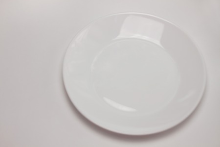 Empty round white plate isolated on white background. Top view, flat lay, copy space, mock up. Table settings, menu, restaurant cuisine.の写真素材