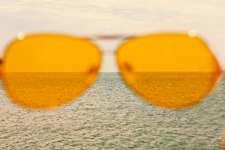 Yellow sunglasses on the sea water and blue sky background. Sunny day, happy vacation, good rest, happiness. Summer view of the sea through the glasses.の写真素材